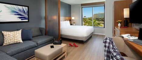 Una habitación de hotel con cama, sofá, escritorio con laptop, televisión y ventana con vista a la ciudad.