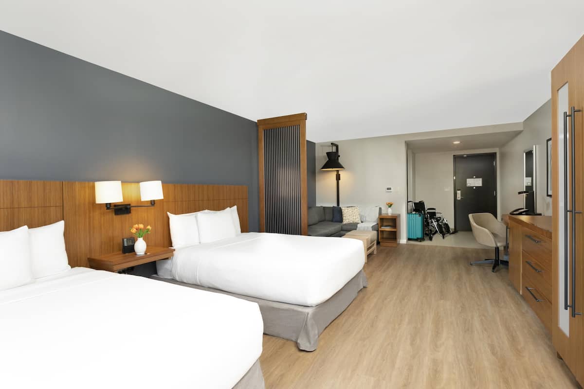 A hotel room with two beds, a desk, a chair, a wardrobe, and a bathroom visible through an open door.