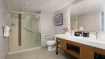 Un baño moderno con ducha envuelta en vidrio, inodoro blanco, tocador de madera y un espejo grande.