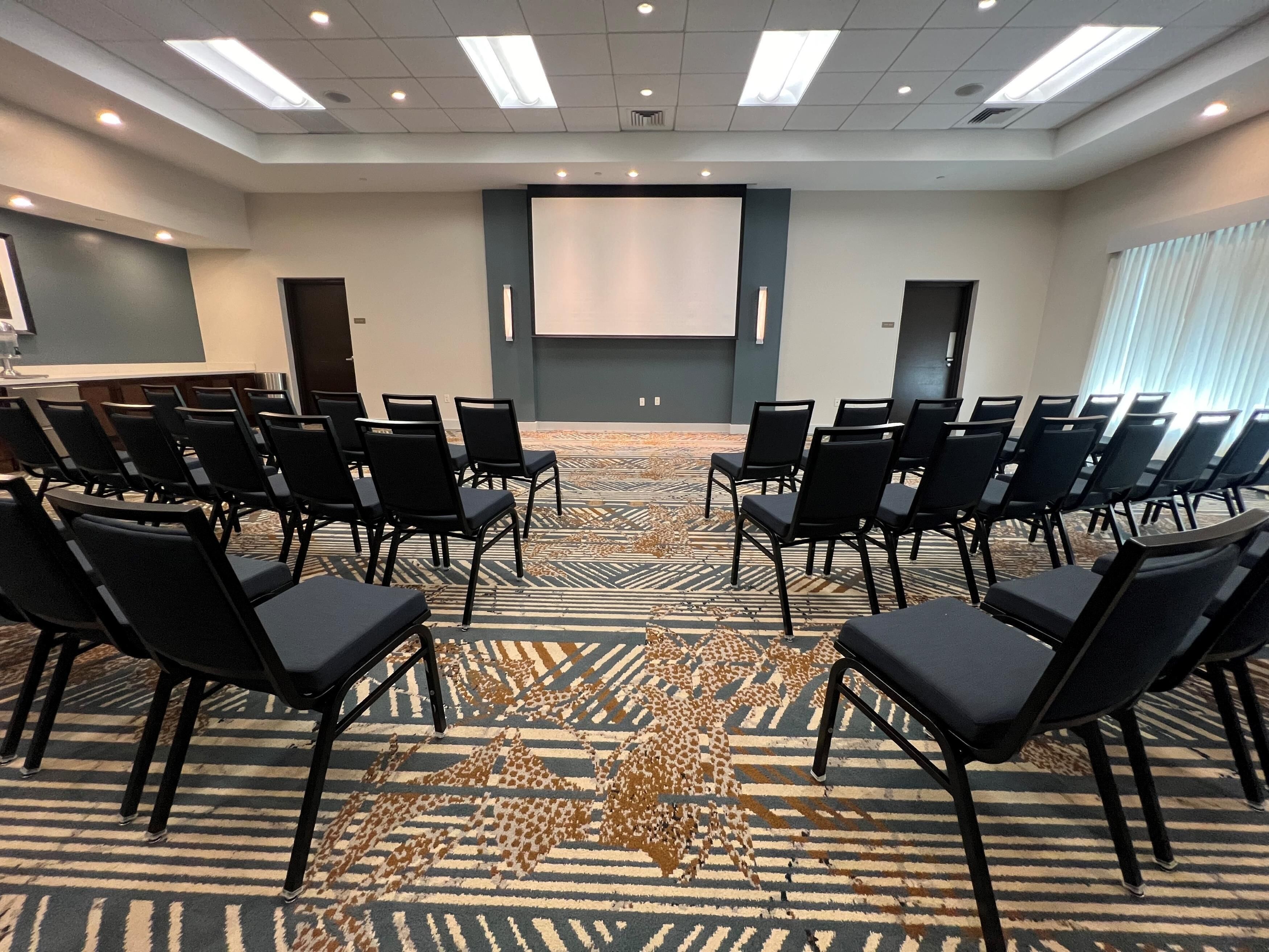 A conference room with rows of chairs, a projector screen, and a carpeted floor.