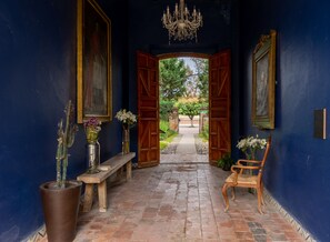 A hallway with a wooden bench, a chair, and a vase with flowers. - Hotel Hacienda San Cristobal (San Francisco del Rincon)