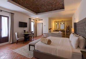 A modern hotel room with a large bed, a desk, a chair, a TV, and a bathroom visible through an open door. - Hotel Hacienda San Cristobal (San Francisco del Rincon)