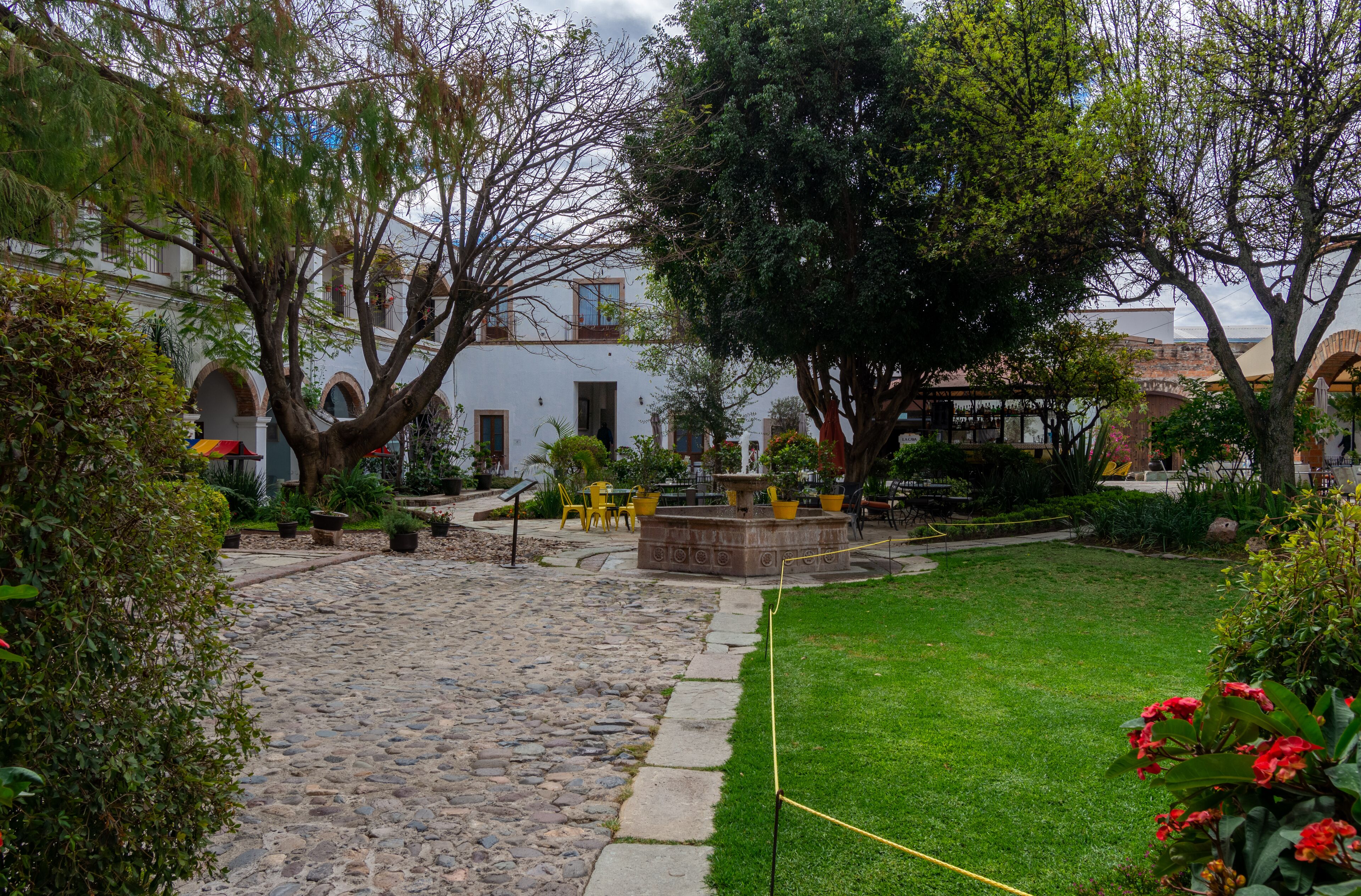 A courtyard with a stone pathway, a fountain, and yellow chairs.