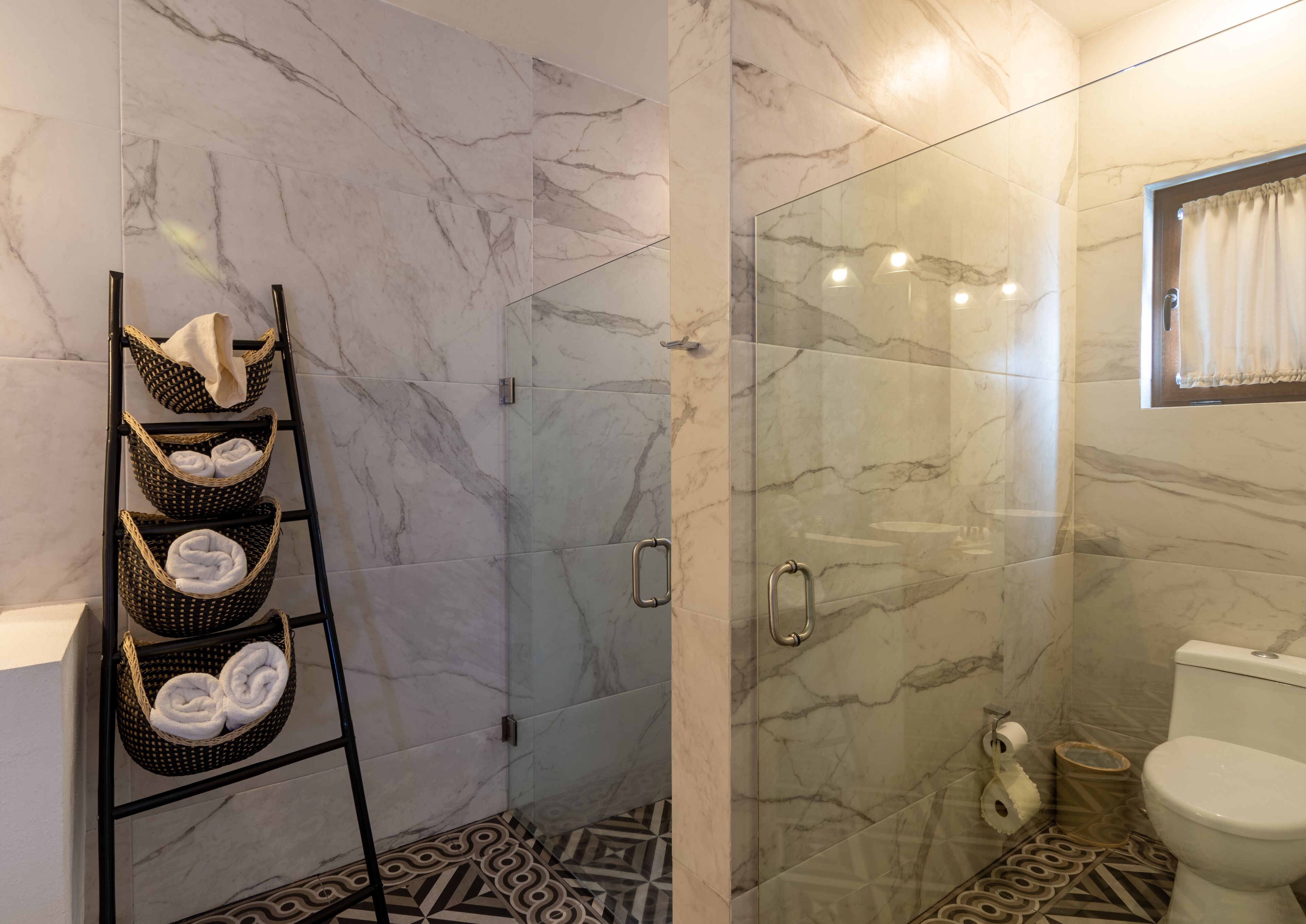 A bathroom with a glass shower enclosure, a toilet, and a towel rack with baskets.