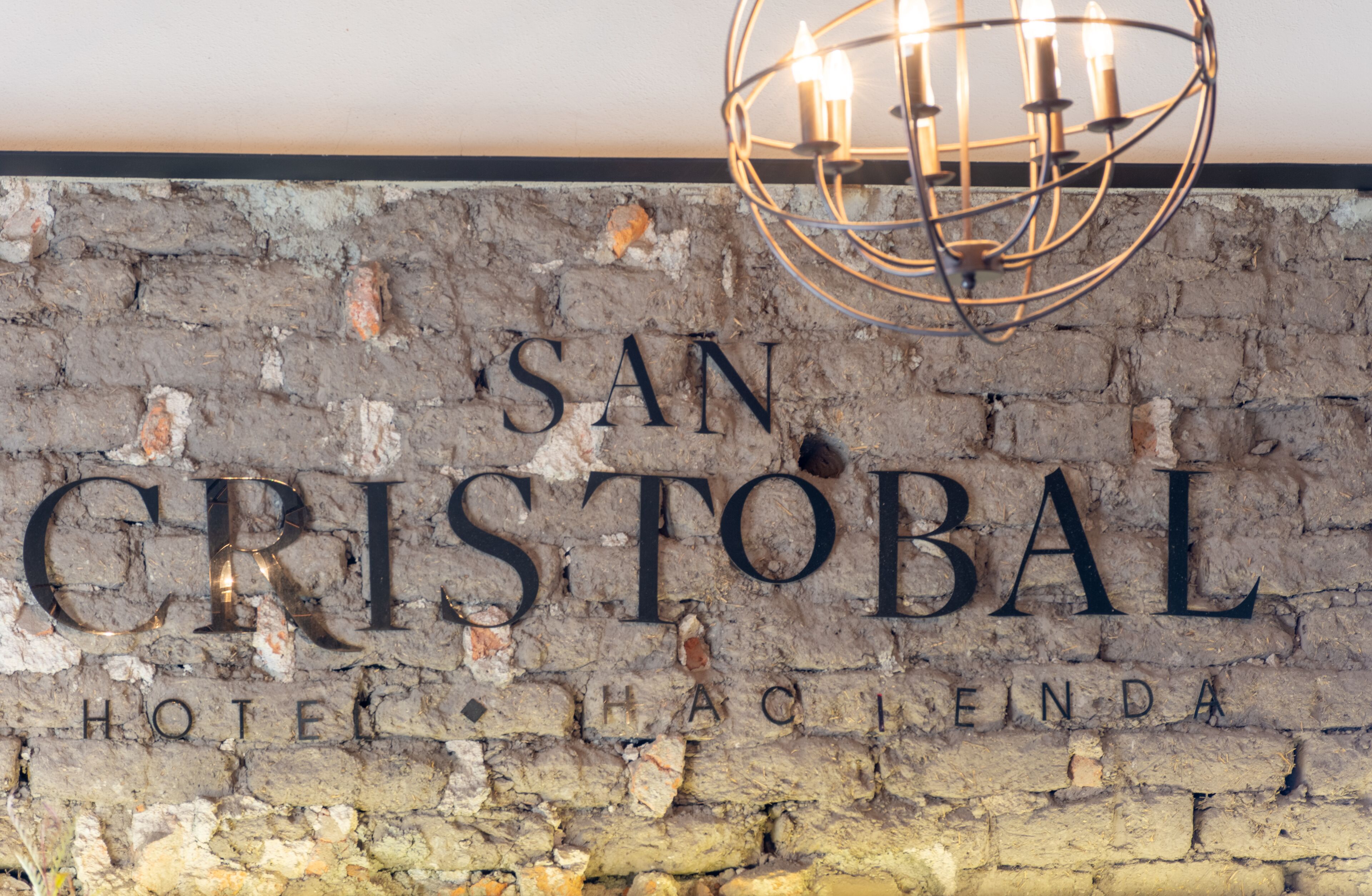 Placa de 'San Cristobal Hotel', com parede de tijolos rústicos e um lustre moderno acima.