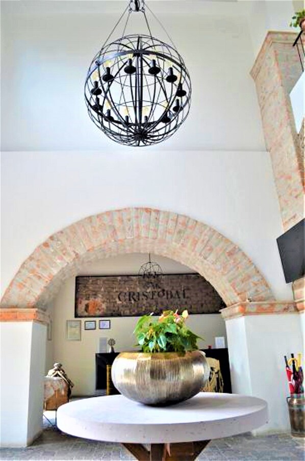 A room with a round table, a hanging spherical light fixture, and a brick archway with a sign above. - Hotel Hacienda San Cristobal (San Francisco del Rincon)