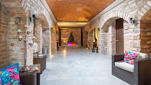 A corridor with brick walls, a Buddha statue, wicker furniture, and a tiled floor.