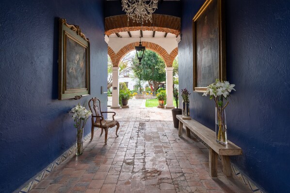 A corridor with a bench, a chair, and a vase with flowers. - Hotel Hacienda San Cristobal (San Francisco del Rincon)