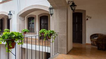 A courtyard with a tiled floor, potted plants, a railing, and a door.