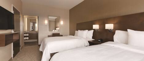 A hotel room with two beds, a TV, a mirror, and a small kitchenette.