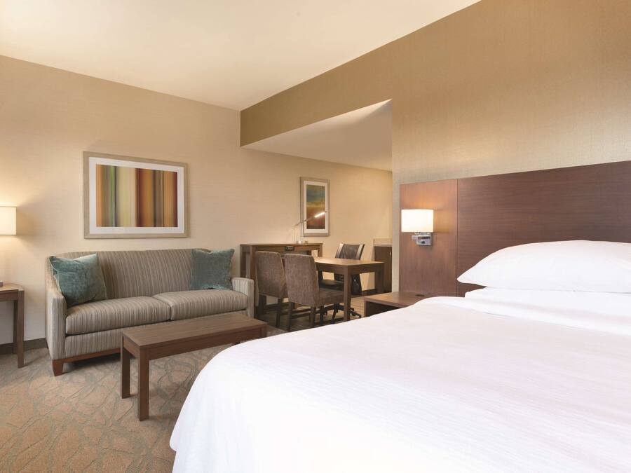 A hotel room with a large bed, a sofa, a desk, and a chair.