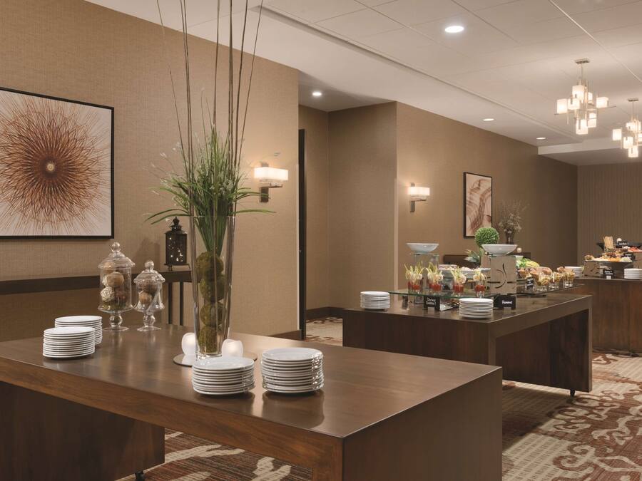 A hotel lobby with a reception desk, buffet area, and a large dining table with stacked plates and a vase of flowers.