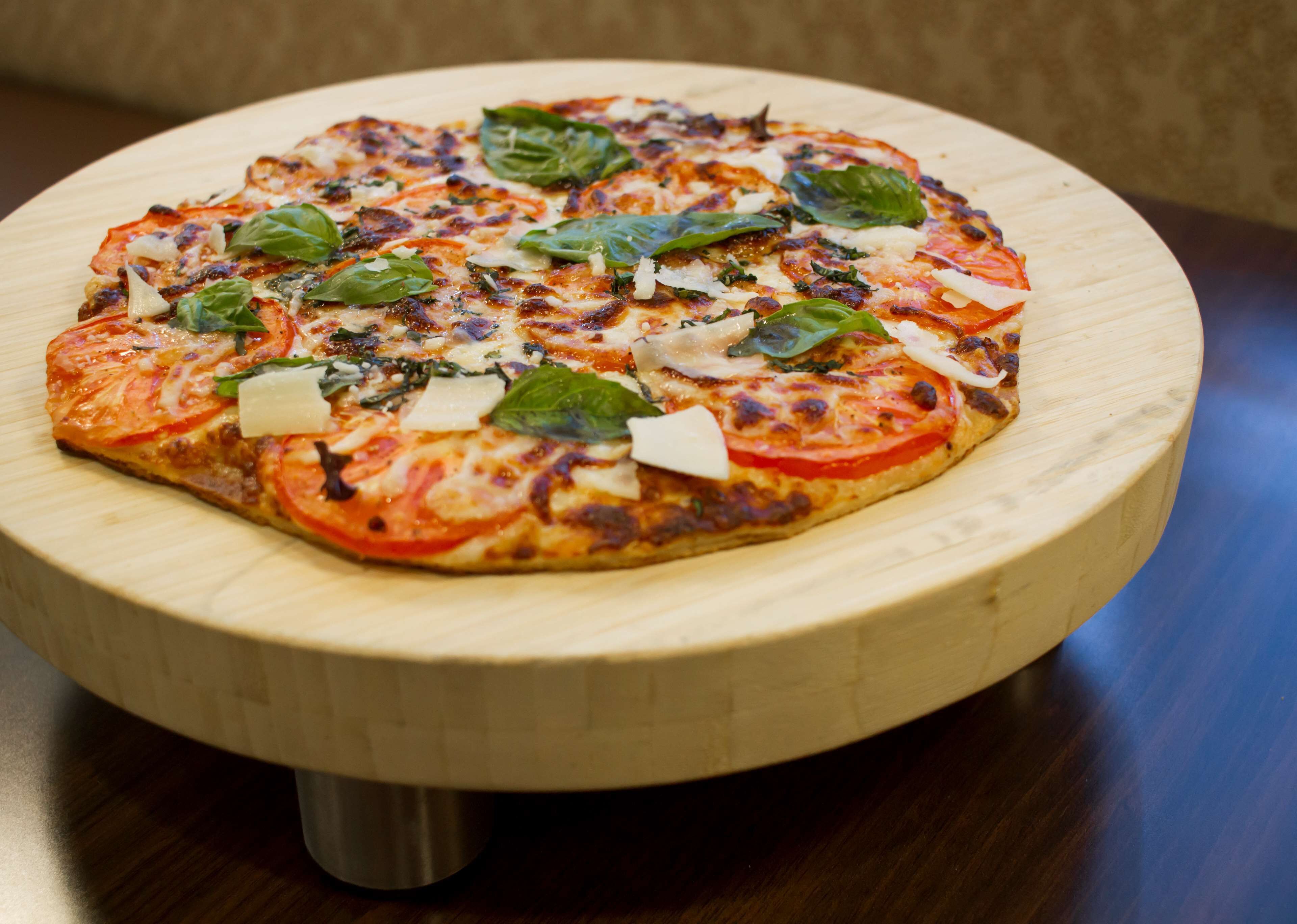 A pizza on a wooden board with a metal stand.