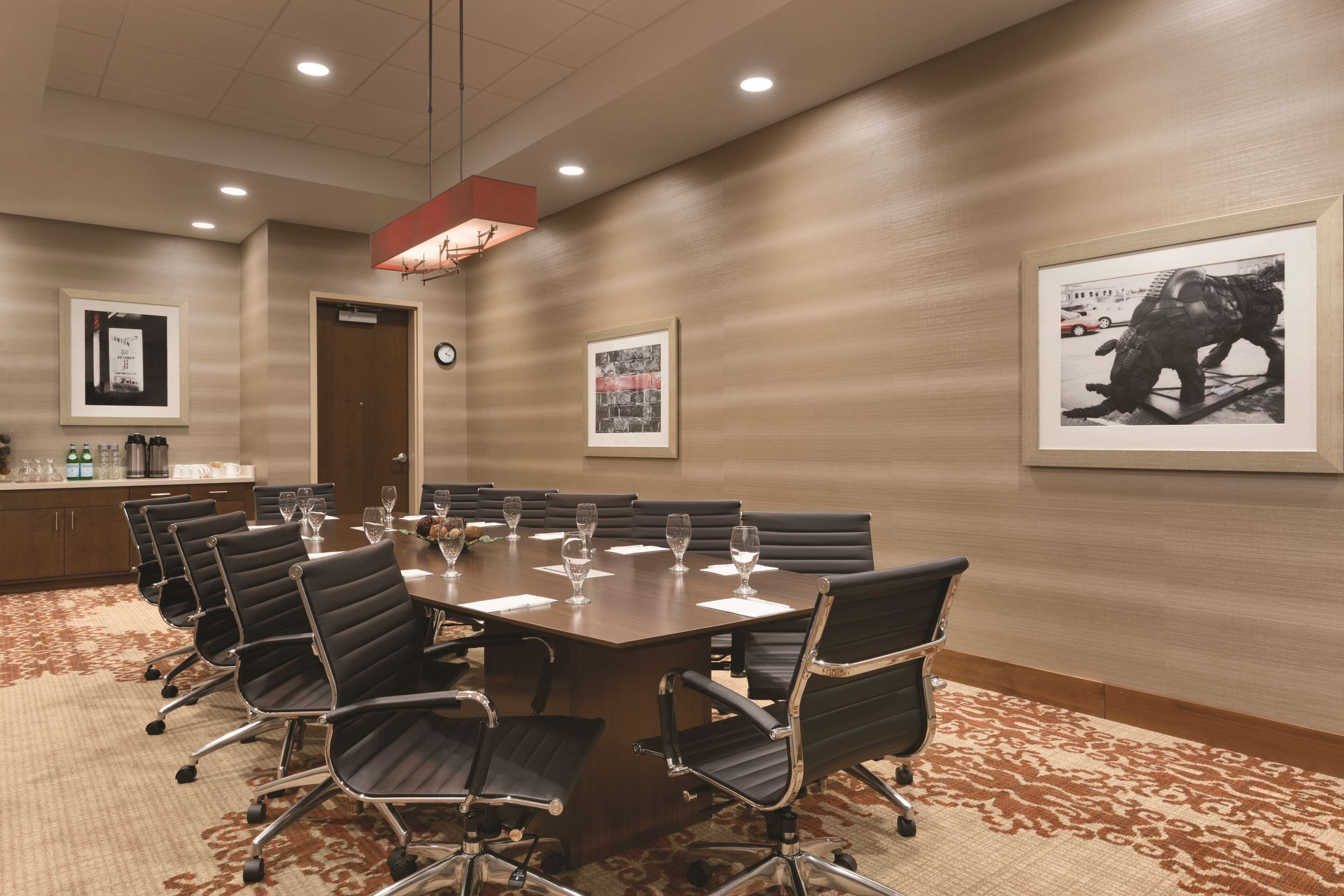 A conference room with a large table, black chairs, and framed pictures on the walls.