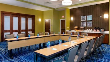 A conference room with a long table, chairs, water bottles, and a coffee station.