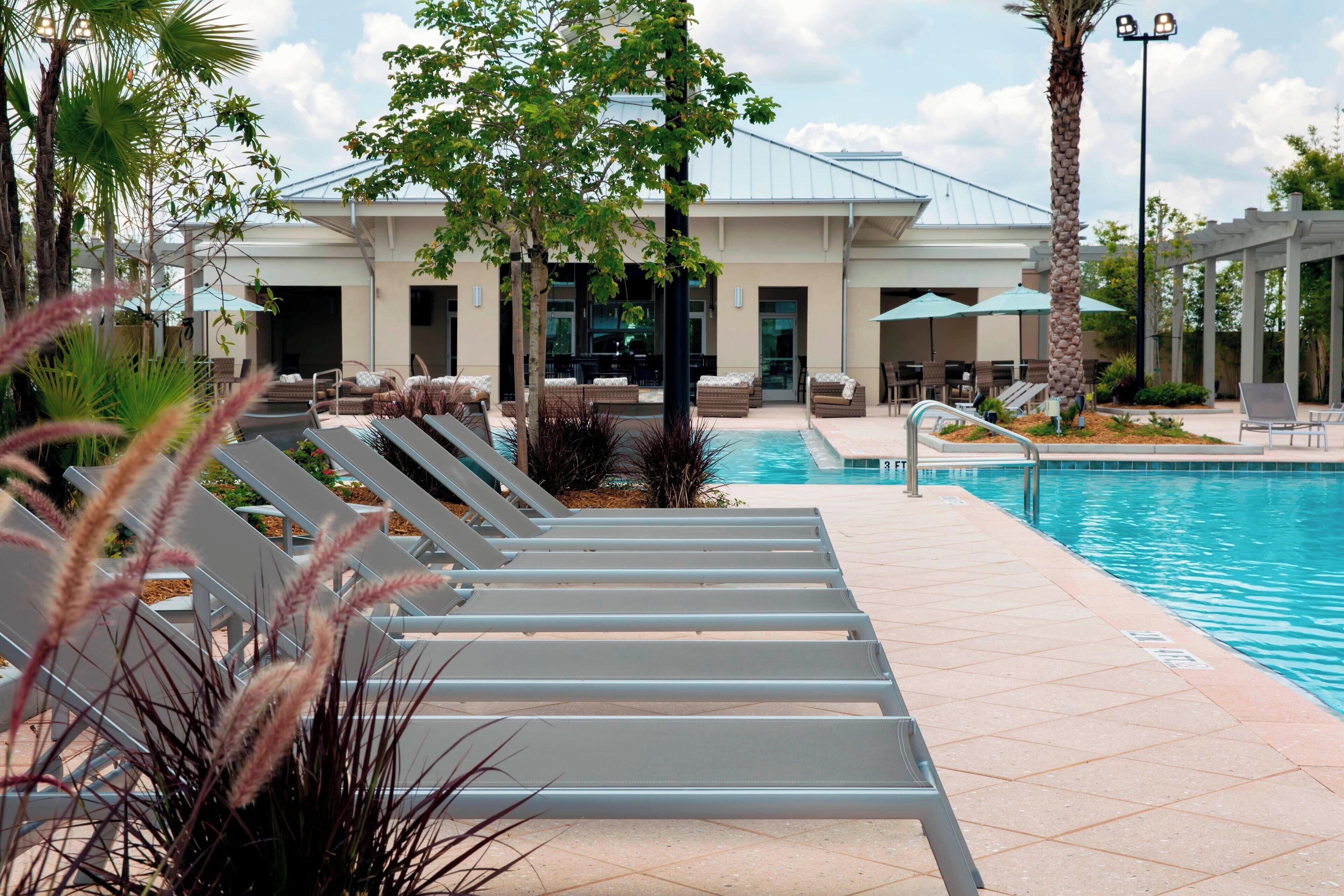 A poolside area with lounge chairs, a pool, and a building with large windows and a covered patio.