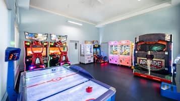Een overdekte speelhal met diverse speelautomaten, waaronder een groot hockey tafel, en een plafondventilator.