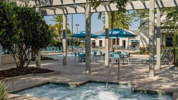 Un área de piscina con un jacuzzi, sillas de descanso y sombrillas.