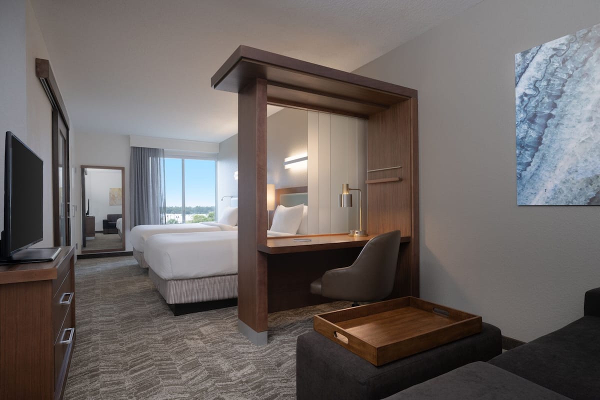 Une chambre d’hôtel avec un lit, un bureau, une chaise, une télévision et une grande fenêtre.