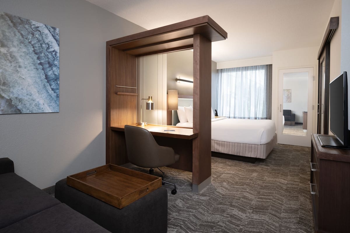 Une chambre d’hôtel équipée d’un bureau, d’un lit, d’une télévision et d’une grande fenêtre.