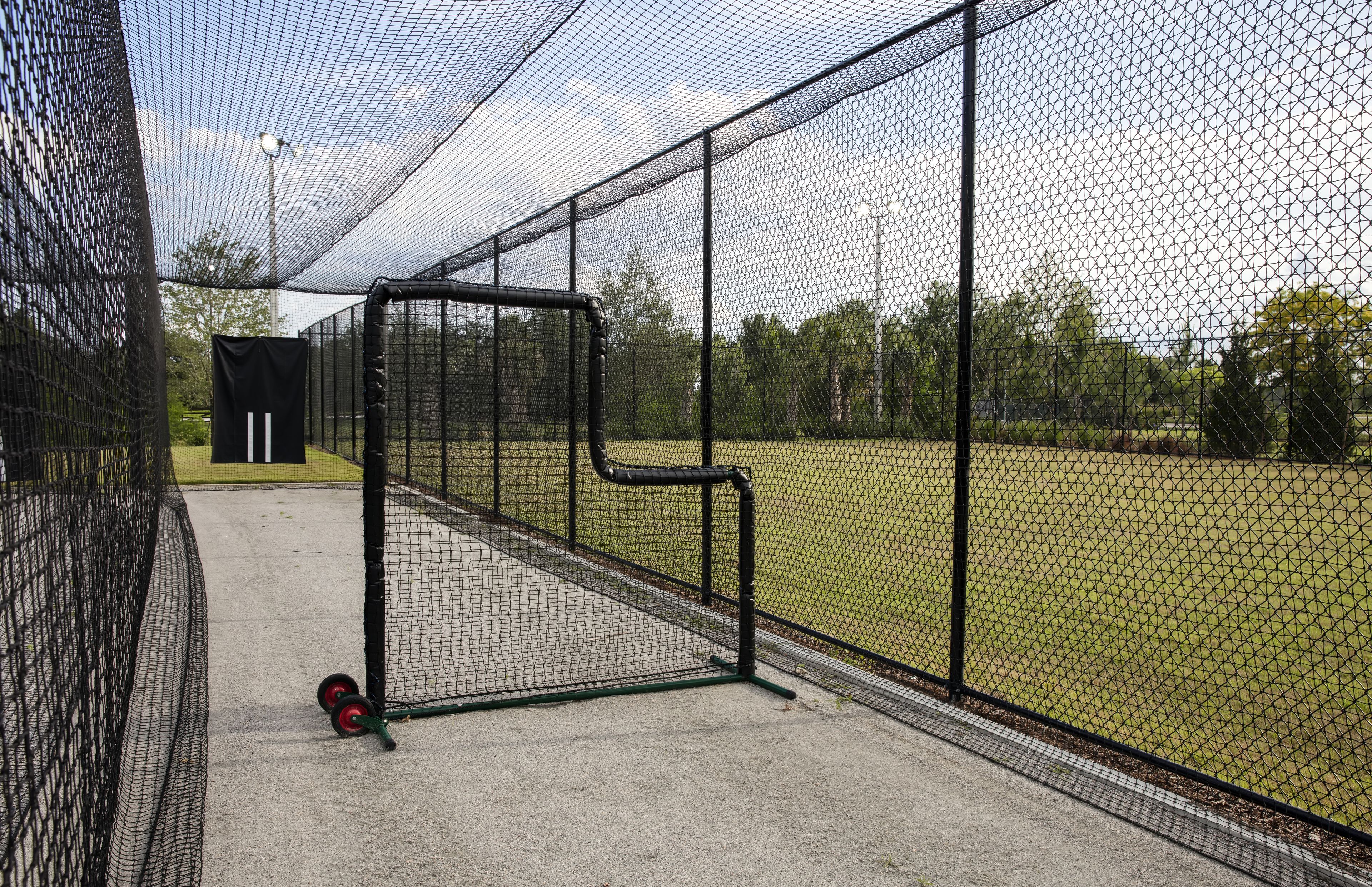 A baseball batting cage with a netted enclosure, a batting tee, and a green cart with red wheels.