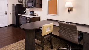 Habitación de hotel compacta con kitchenette, una mesa de comedor, una silla, un escritorio con silla y una lámpara de pared.