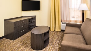Habitación de hotel con televisor de pantalla plana montado en la pared, un sofá, una mesita redonda y un minibar.