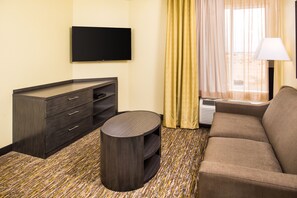 A hotel room with a flat-screen TV mounted on the wall, a sofa, a small round table, and a minibar. - Candlewood Suites Carlsbad South by IHG (Carlsbad)