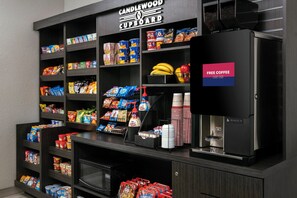 A kitchenette area with shelves stocked with snacks, a coffee machine, and a sign offering free coffee. - Candlewood Suites Carlsbad South by IHG (Carlsbad)