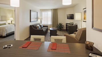 A hotel room with a bed, a sofa, a dining table with placemats, a TV, and a desk with a phone and remote control.