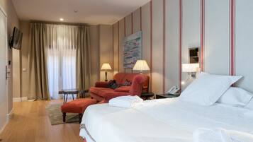 A hotel room with a large bed, a red armchair, a small table, and a TV mounted on the wall.