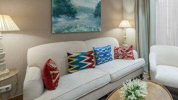 Un salon avec un canapé blanc, des coussins colorés, un tableau accroché au mur et une lampe posée sur une table d’appoint.