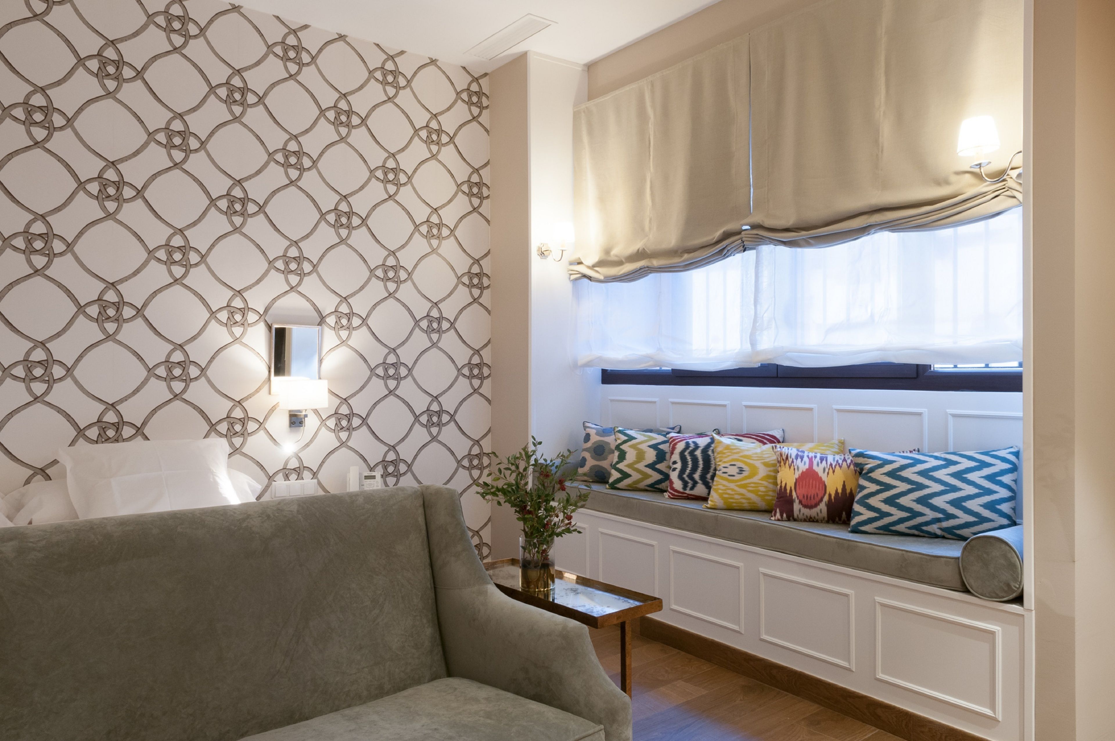 Un salon chaleureux avec un papier peint à motifs, un canapé, une fenêtre avec des rideaux et une petite table sur laquelle est posée une plante.