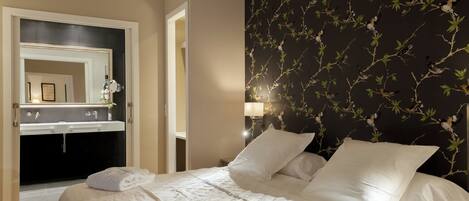 A hotel room with a bed, white linens, a bathroom with a mirror, and a wall with a bird pattern.