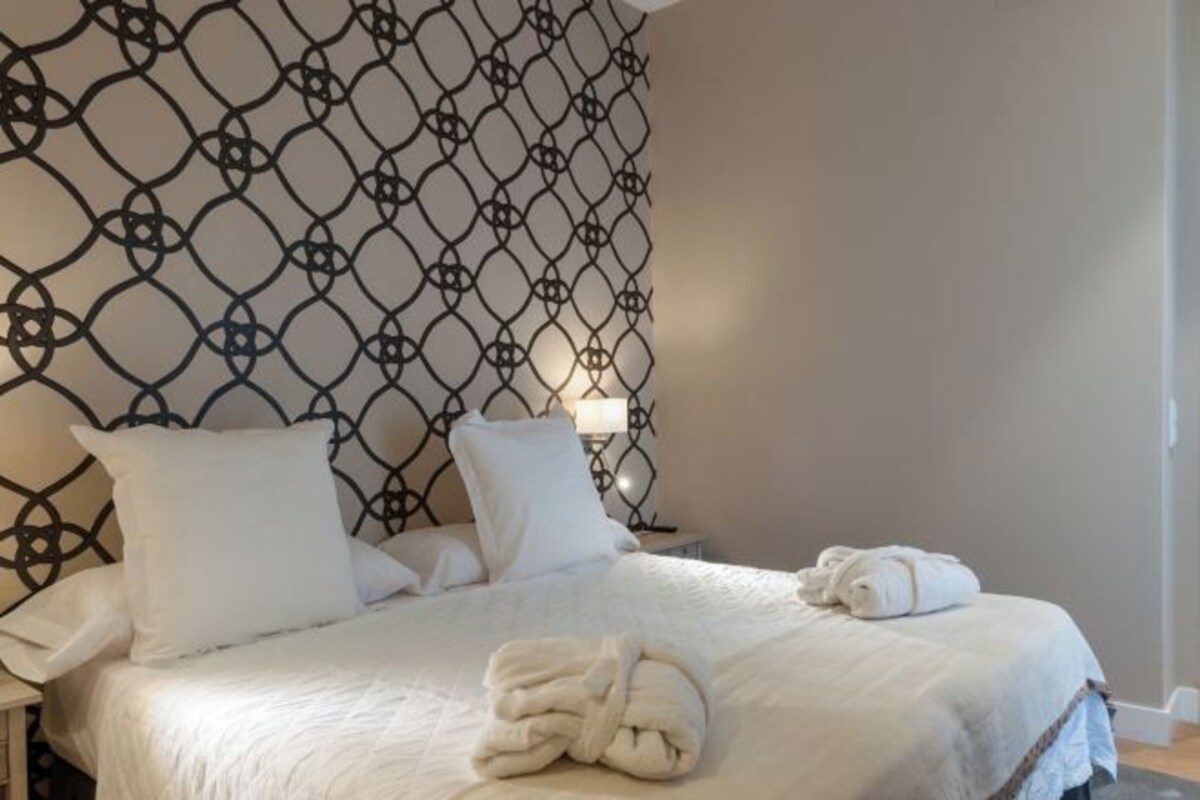 A neatly made bed with white linens and a folded towel on the side.