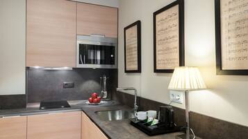 A modern kitchen with a built-in microwave, stainless steel sink, and a kettle. There are framed musical sheets on the wall and a lamp on the counter.