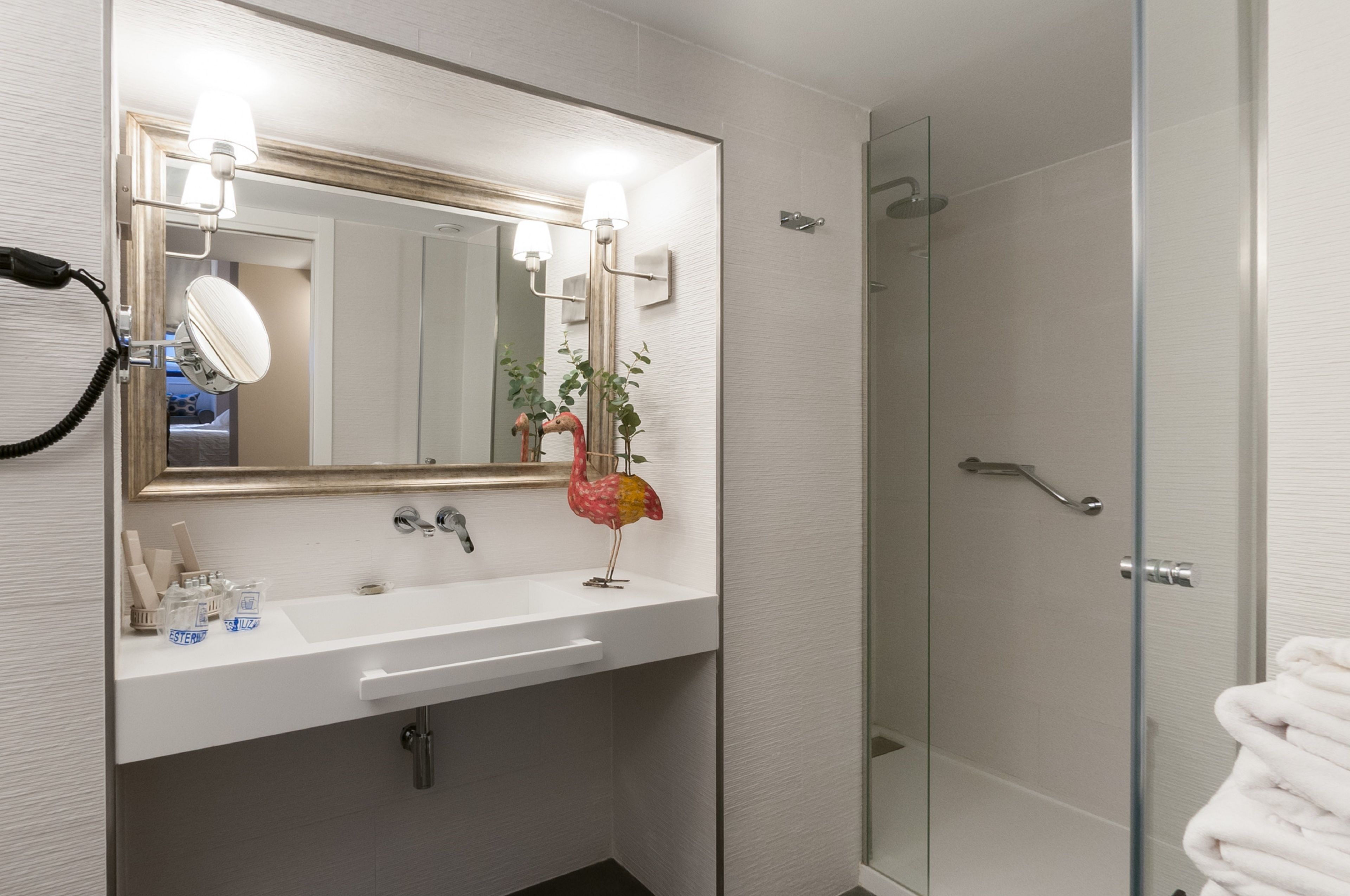 Un baño con lavamanos blanco, un espejo iluminado, ducha y perchero.