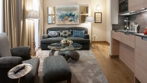 A modern living room with a sofa, ottoman, and coffee table, a kitchen with a microwave and sink, and artwork on the walls.