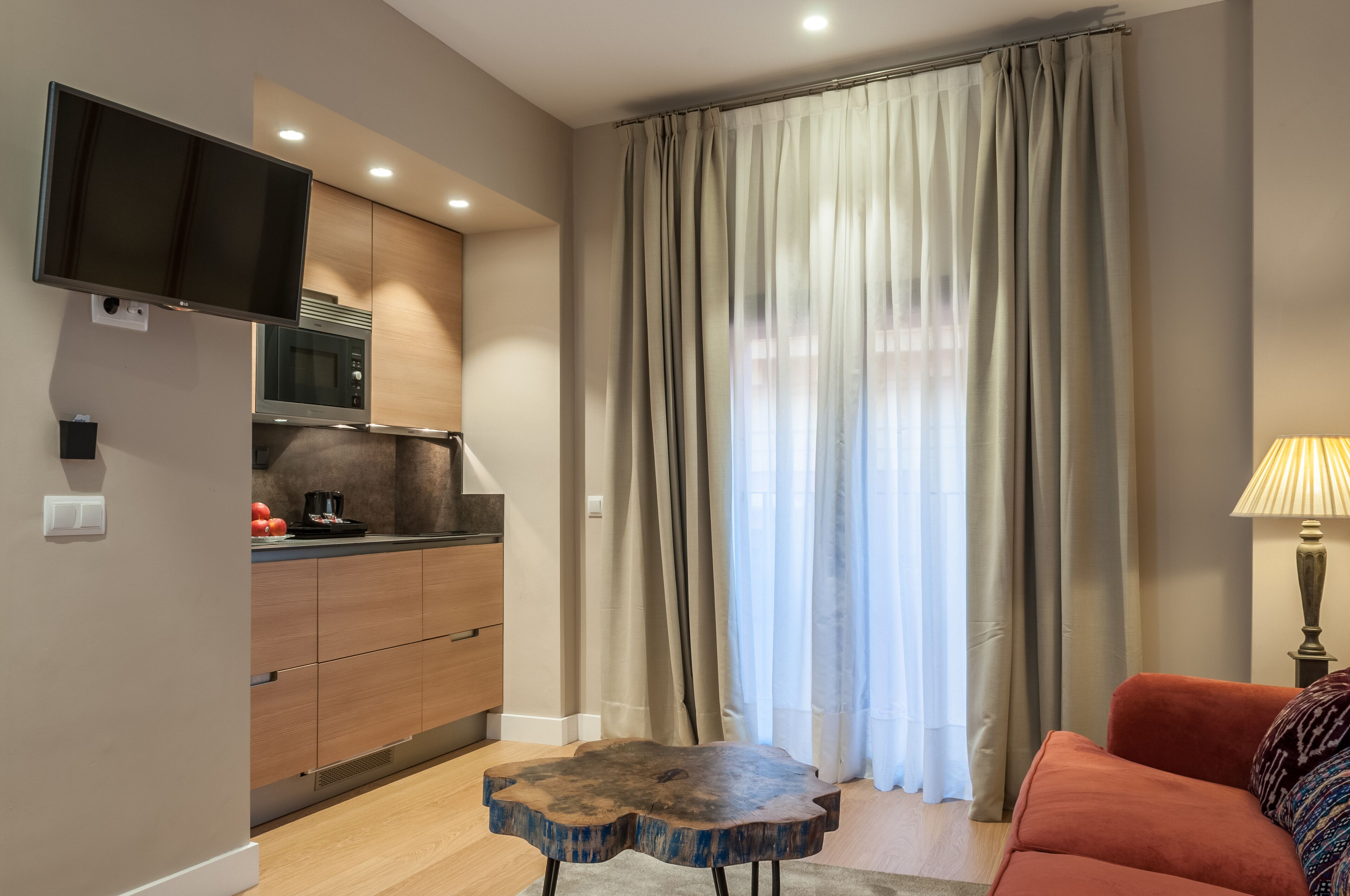 A modern kitchen with built-in appliances, a flat-screen TV, and a dining area with a wooden table and red sofa.
