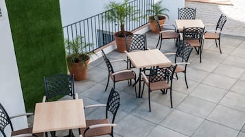 Una terraza con mobiliario exterior, plantas en macetas y un muro cubierto de vegetación.