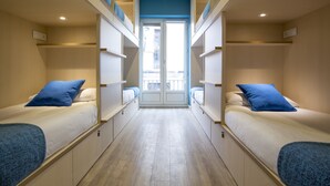 A corridor leading to a balcony with two beds on either side, each with a blue pillow and a blue blanket. - Mola Hostel (Madrid)