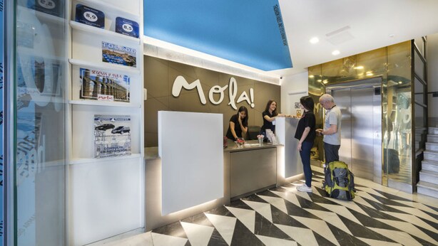 A reception area with a counter, a sign reading "Mola!", and a patterned floor. - Mola Hostel (Madrid)