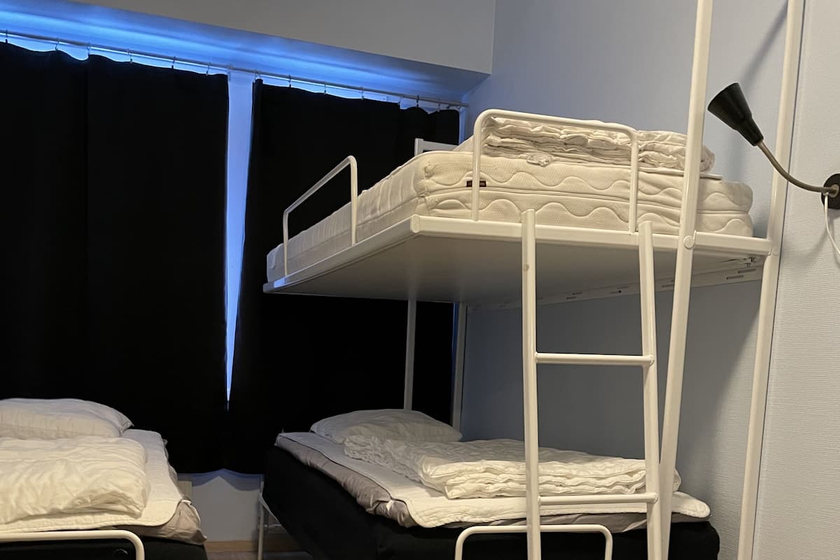 Habitación con literas, una escalera, cortinas en la ventana y una lámpara de noche.