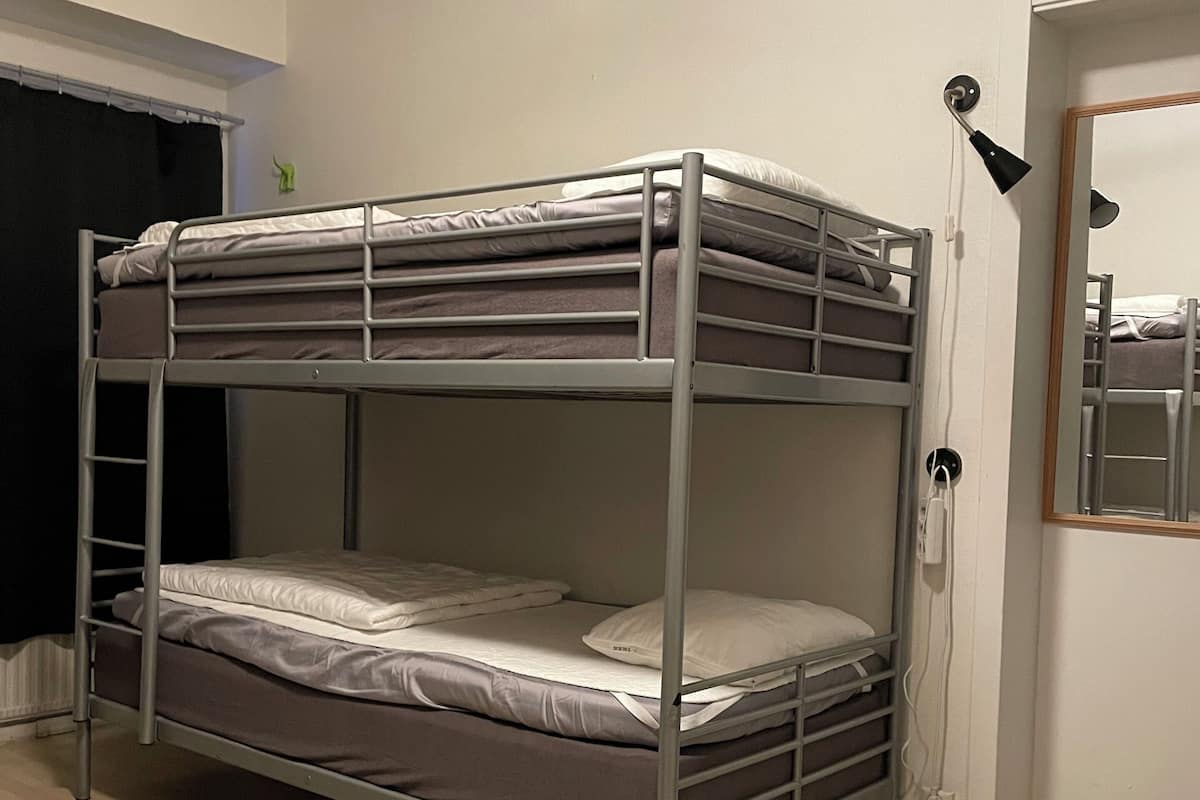 Una cama litera con una silla de madera y una mesa en una habitación con paredes blancas y una puerta.