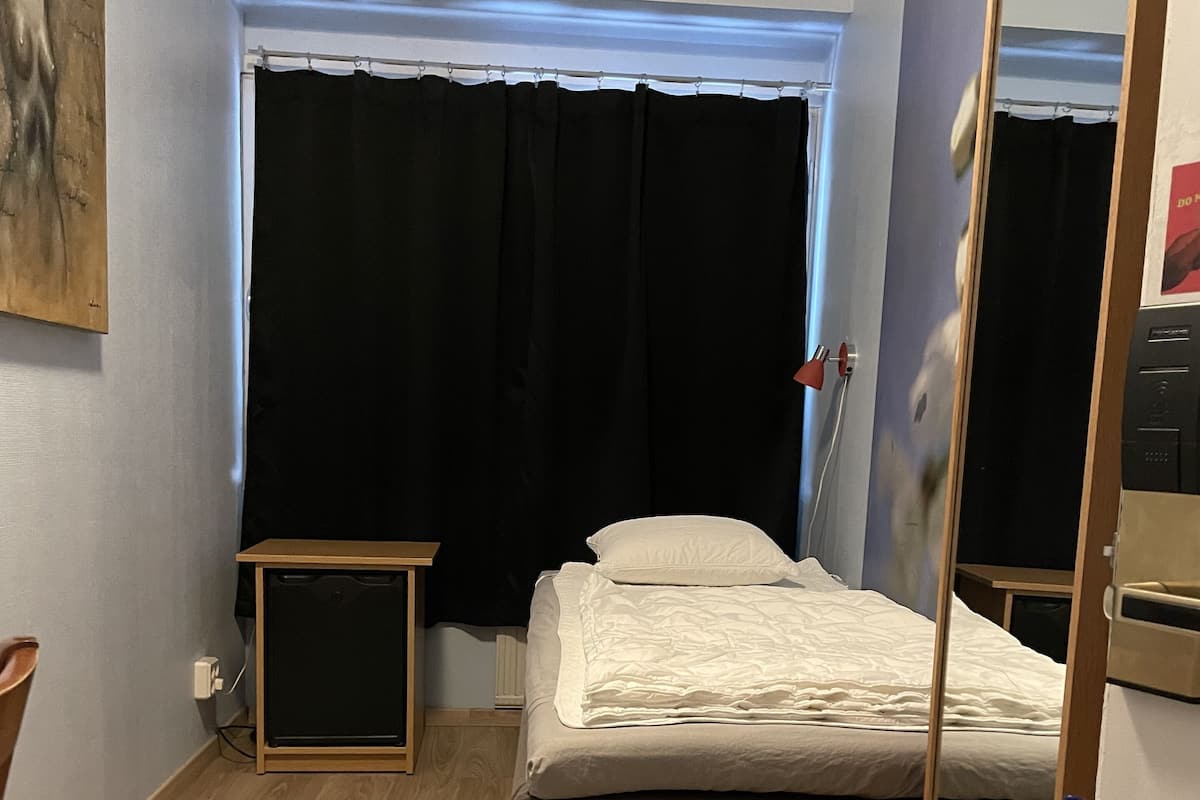 Un dormitorio pequeño y ordenado con una cama individual, una mesita y un espejo.