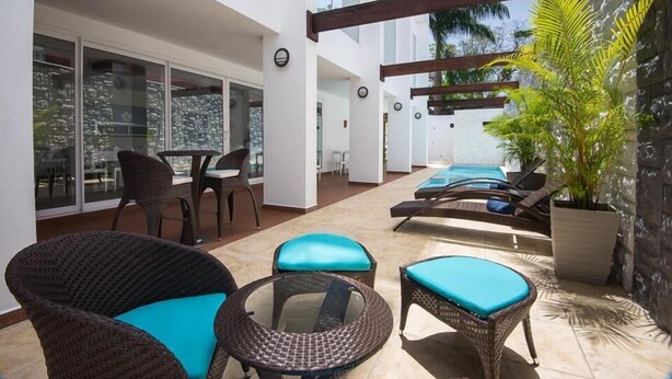 A modern outdoor patio with wicker furniture, a glass table, and a pool area. - Hotel Latitud 15 (San Pedro Sula)