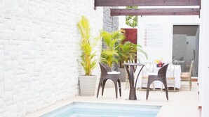A poolside area with a white brick wall, potted plants, wicker chairs, and a table. - Hotel Latitud 15 (San Pedro Sula)