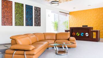 A modern lobby with a leather sectional sofa, a glass coffee table, and decorative panels on the wall.