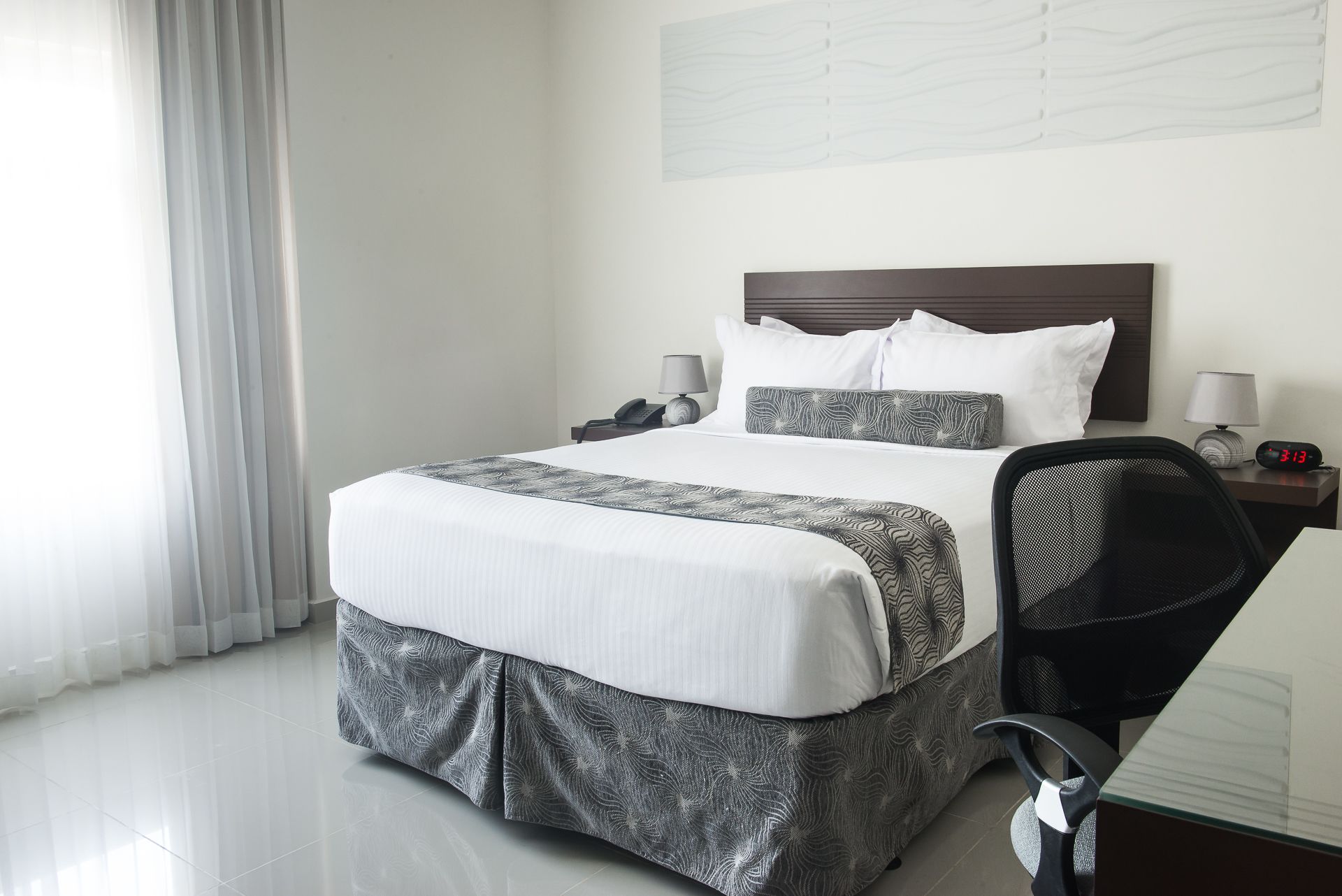Una cama bien hecha con una colcha estampada, una mesita de noche con lámpara y una silla.