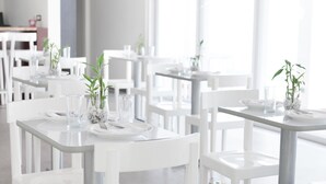 A modern dining area with white tables and chairs, each set with plates, cutlery, and glassware. - Hotel Latitud 15 (San Pedro Sula)